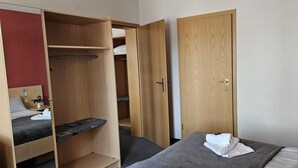 A hotel room with a bed, a wooden wardrobe, and a bedside table.
