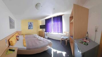 A hotel room with a bed, a desk, a chair, a television, and a window with curtains.