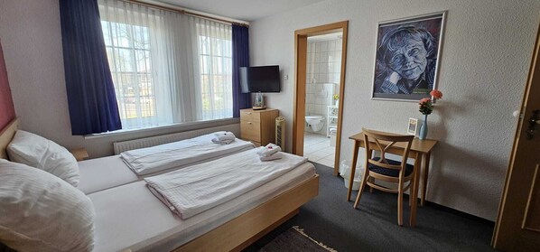 A hotel room with two beds, a desk, a chair, a television, and a bathroom visible through an open door. - Tropicana Lüneburger Hof (Munster im Heidekreis)