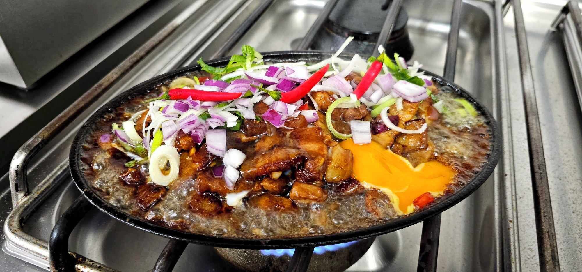 A hot pot meal with various ingredients and garnishes on a stove.