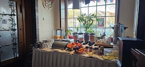 A breakfast buffet with various food items, a coffee machine, and a large window with a view of the street.