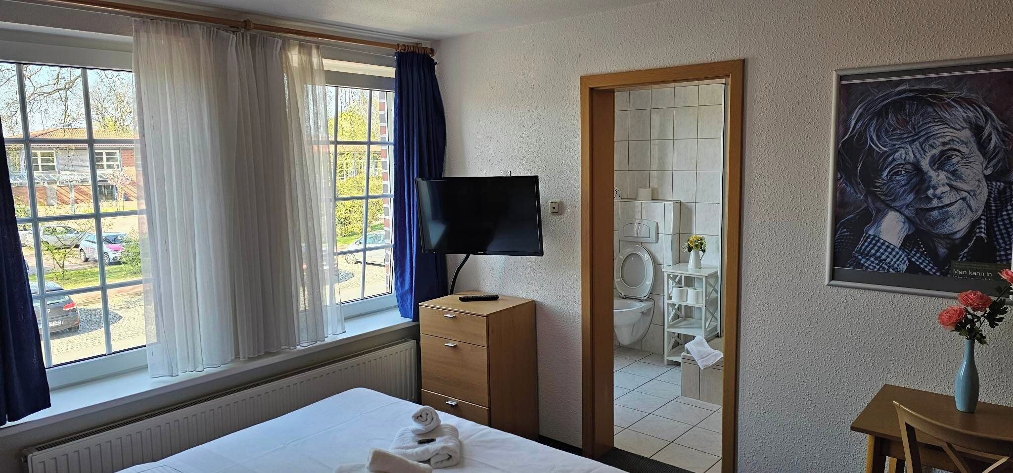 Une chambre d’hôtel avec un lit, une télévision, un miroir et une fenêtre avec des rideaux.