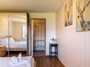A hotel room with a bed, a mirror, a wooden wardrobe, a small table with a vase, and a painting on the wall.