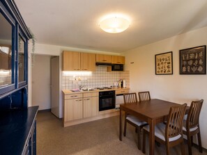 A compact kitchen with wooden cabinets, a microwave, and a dining area with a table and chairs. - Luna Appartement/Fewo 2-4 Bettwohnung by Interhome (Gwatt (Thun))
