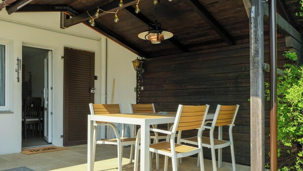 An outdoor patio with a table and chairs, a door, and a wooden wall. - Luna Appartement/Fewo 2-4 Bettwohnung by Interhome (Gwatt (Thun))
