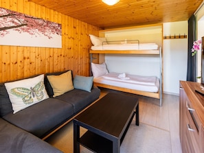 A room with a bunk bed, a sofa, a table, and a wooden wall with a cherry blossom painting. - Luna Appartement/Fewo 2-4 Bettwohnung by Interhome (Gwatt (Thun))