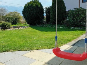 A swing set in a garden with a lawn, trees, and a stone wall.