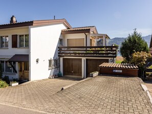 Une maison à deux étages avec un garage, un balcon agrémenté de plantes et une vue sur les montagnes.
