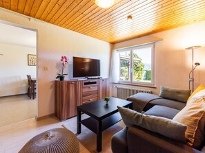 Un salon moderne avec une télévision, un canapé, une table basse et une vue sur la verdure à l’extérieur.