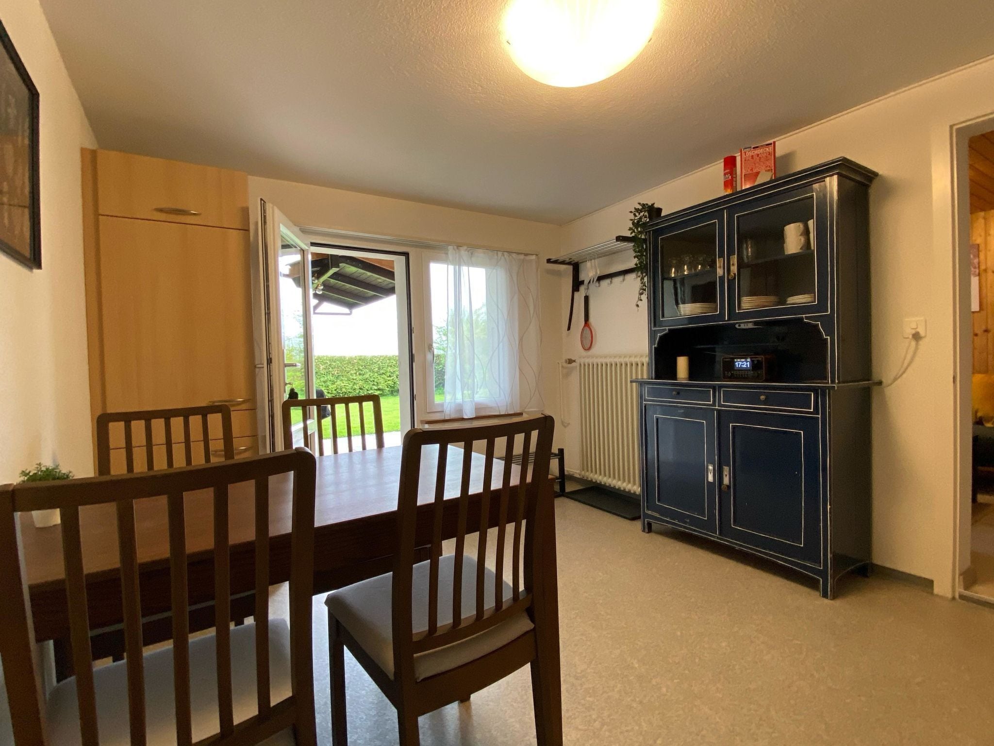 A dining area with a table and chairs, a kitchen area with cabinets, and a view of the outdoors through a door.