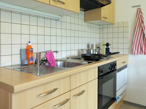 A kitchen with a sink, a stove, and a kettle. There is a bottle of dish soap and a pink towel hanging on the faucet. - Luna Appartement/Fewo 2-4 Bettwohnung by Interhome (Gwatt (Thun))