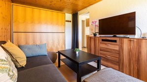 A modern room with a wooden ceiling, a sofa, a small table with a plant, and a TV on a wooden cabinet. - Luna Appartement/Fewo 2-4 Bettwohnung by Interhome (Gwatt (Thun))