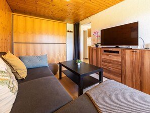 A modern room with a wooden ceiling, a sofa, a small table with a plant, and a TV on a wooden cabinet. - Luna Appartement/Fewo 2-4 Bettwohnung by Interhome (Gwatt (Thun))