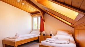 A room with two wooden beds, a window with curtains, and a wooden ceiling. - Hauswurz Appartement/Fewo Appartement/Fewo by Interhome (Gwatt (Thun))
