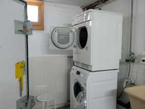 A laundry room with stacked washers and dryers, a small stool, and a window. - Hauswurz Appartement/Fewo Appartement/Fewo by Interhome (Gwatt (Thun))