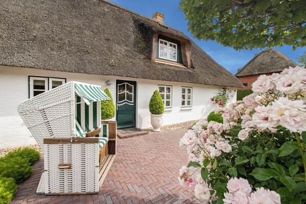 Ein traditionelles Haus mit Strohdach, weißer Fassade, grüner Tür und einem kleinen Vorgarten mit Rosen.
