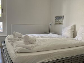 A neatly made bed with white linens and towels, a bedside table with a lamp, and a painting on the wall. - Seewohnung 2 Appartement/Fewo Appartement/Fewo by Interhome (Spiez)