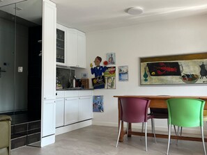 A modern kitchen with white cabinets, a dining area with a wooden table and colorful chairs, and various wall art.