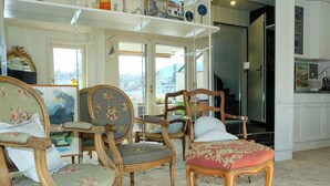 Quarto com móveis de estilo antigo, incluindo cadeiras e uma mesa, uma janela grande com vista e uma área de cozinha.