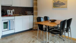 Eine Küche mit weißen Schränken, einem Herd und einer Kaffeemaschine. Es gibt einen Esstisch mit vier Stühlen und ein Bild an der Wand.