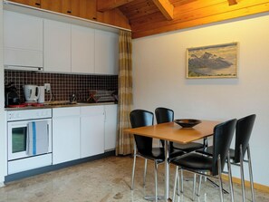 Eine Küche mit weißen Schränken, einem Herd und einer Kaffeemaschine. Es gibt einen Esstisch mit vier Stühlen und ein Bild an der Wand.