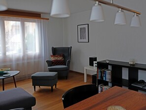 A modern living room with a grey armchair, a wooden dining table, and a bookshelf. - Ambiente Appartement/Fewo Appartement/Fewo by Interhome (Spiez)