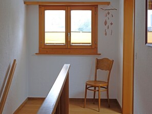 Ein Zimmer mit Holzfenster, einem Stuhl und einer Holztreppe.