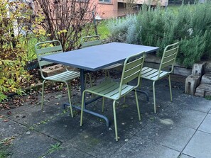 Eine Terrasse mit Tisch und Stühlen, umgeben von Pflanzen und einem Zaun.