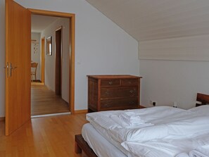 A bedroom with a wooden dresser, a bed with white bedding, and a hallway leading to another room. - Ambiente Appartement/Fewo Appartement/Fewo by Interhome (Spiez)