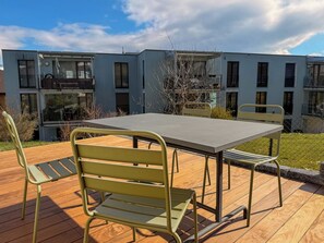 A deck with a table and chairs, a modern building in the background, and a clear sky. - Ambiente Appartement/Fewo Appartement/Fewo by Interhome (Spiez)