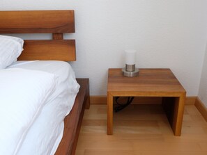 Ein Schlafzimmer mit einem hölzernen Kopfende, einem Nachttisch aus Holz mit einer weißen Kerze und einem Holzboden.