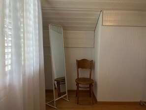 Ein Zimmer mit einem Holzstuhl, einem großen Spiegel und einem weißen Vorhang.