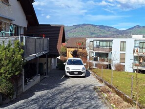 A gravel driveway leading to a white car parked in front of a building with a sloped roof and a balcony. - Ambiente Appartement/Fewo Appartement/Fewo by Interhome (Spiez)