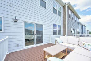 Eine überdachte Terrasse mit einer Couch und einem Tisch, eine Schiebetür aus Glas und eine weiße Fassade.