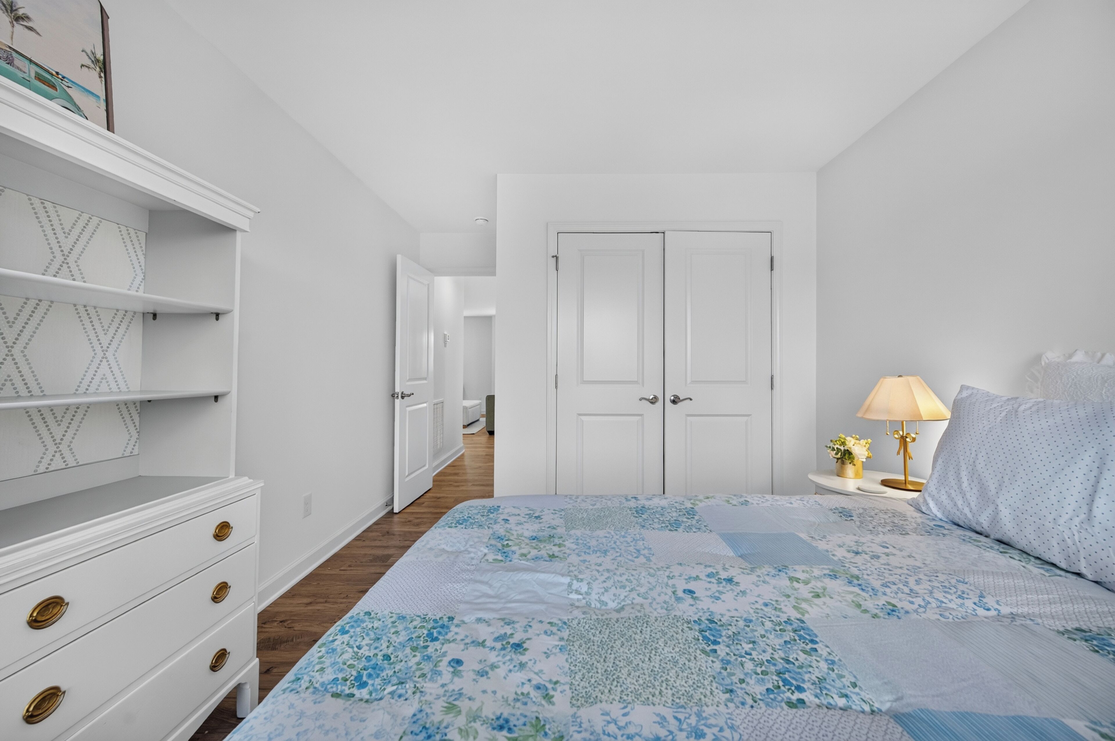 Un dormitorio con cama, mesita de noche, lámpara, cómoda y puerta.