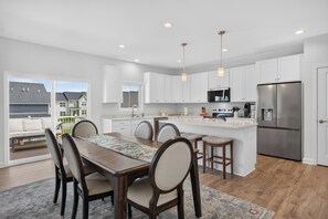 A modern kitchen with white cabinets, a stainless steel refrigerator, and a dining area with a wooden table and chairs. - Enjoy a spacious multi-level townhome just minutes from Virginia Tech, featuring an open-concept layout, a gourmet kitchen, a private deck, and seasonal access to the community pool. (Blacksburg)