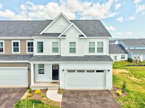 A two-story house with a garage, a front porch, and a well-maintained lawn. - Enjoy a spacious multi-level townhome just minutes from Virginia Tech, featuring an open-concept layout, a gourmet kitchen, a private deck, and seasonal access to the community pool. (Blacksburg)