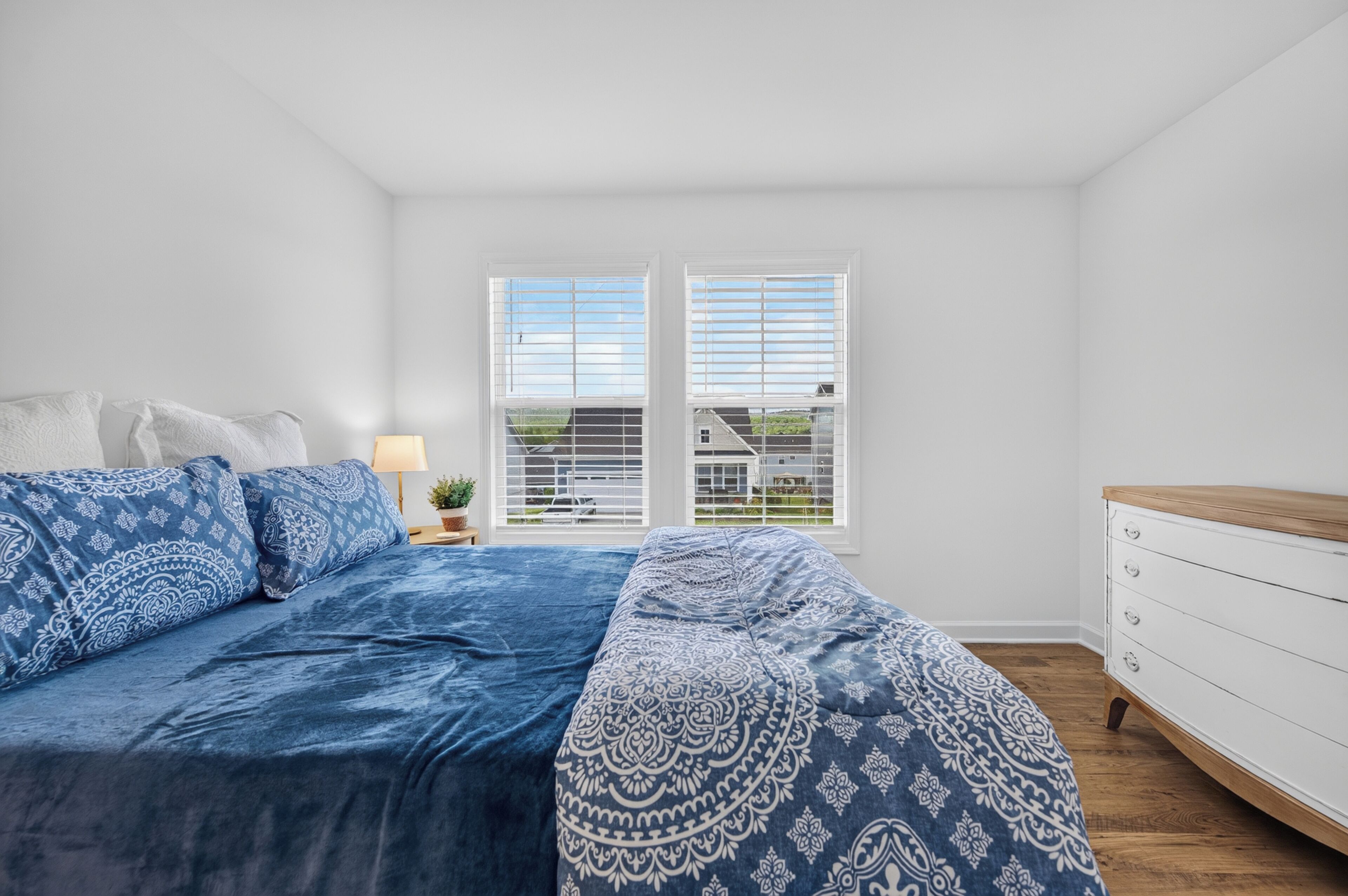 A bedroom with a bed, a nightstand, a lamp, and a dresser.