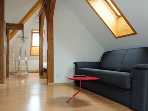 A modern loft with exposed wooden beams, a gray sofa, a red table, and a skylight. - Spatzennest Appartement/Fewo Studio by Interhome (Spiez)