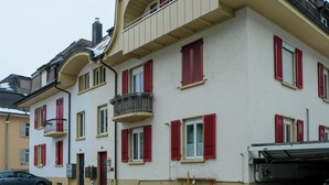 Un edificio de varios pisos con contraventanas rojas, un balcón y un garaje.