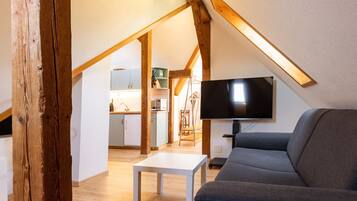 Une pièce de style « loft » avec une poutre en bois, un téléviseur à écran plat, un canapé gris et une table blanche.