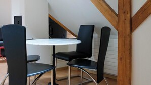 Un pequeño comedor con una mesa redonda y dos sillas, vigas de madera en el techo y una escalera al fondo.