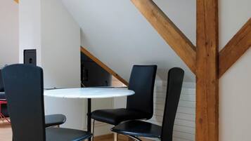 Un petit coin repas avec une table ronde et deux chaises, des poutres en bois au plafond et un escalier en arrière-plan.