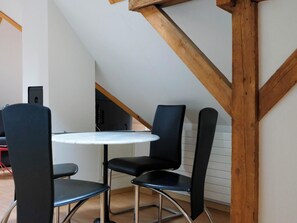 Ein kleiner Essbereich mit einem runden Tisch und zwei Stühlen, Holzbalken an der Decke und einer Treppe im Hintergrund.