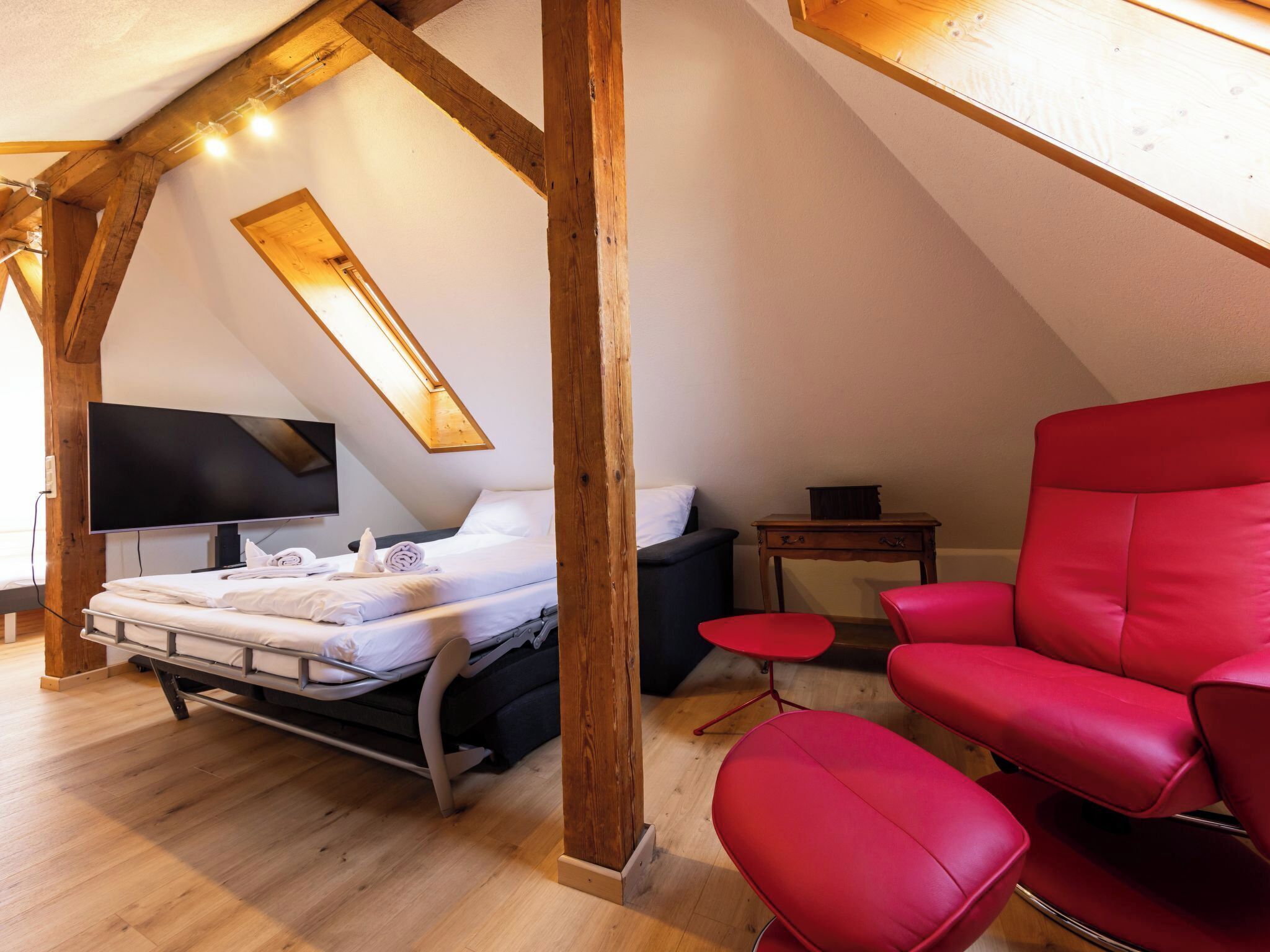 Une chambre à coucher avec un lit, une chaise rouge, une petite table et un téléviseur.