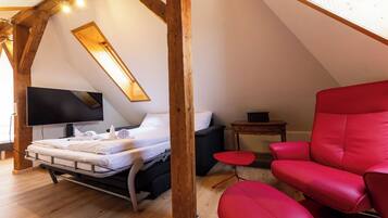 Une chambre à coucher avec un lit, une chaise rouge, une petite table et un téléviseur.