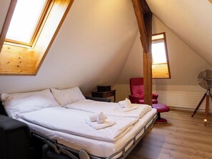 Ein Schlafzimmer mit Bett, einem roten Sessel, einem Ventilator und einer Holzbalkendecke.