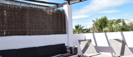 Eine Terrasse im Freien mit einer weißen Bank, einem weißen Tisch und zwei Liegestühlen.