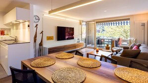 A modern kitchen with a built-in oven, a dining area with a wooden table and woven placemats, a sofa, and a TV mounted on the wall. - Buchtoase Appartement/Fewo 4-Bett Wohnung by Interhome (Spiez)