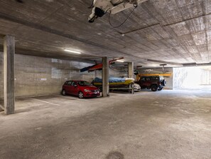 Eine Parkgarage mit Betonwänden, einem roten Auto, einem Boot auf einem Anhänger und einem gelben Fahrzeug.